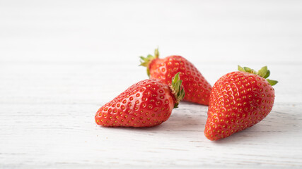 Three ripe strawberries on white wooden table. Isolated strawberry on white background. Summer berry pleasure