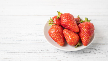 Few ripe strawberries on white small plate on wooden table Isolated strawberry bowl on white background Summer pleasure