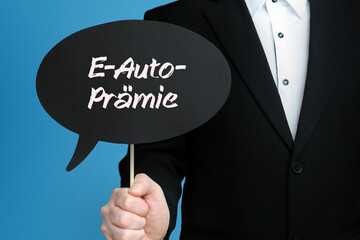 E-Auto-Prämie. Mann im Anzug hält Sprechblase in der Hand. Der Text E-Auto-Prämie steht im Schild. Blauer Hintergrund. Geschäftsmann für Business, Finanzen, Statistik