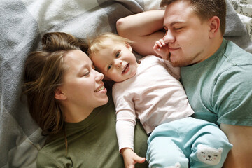 Top view of happy family in bed in the morning in casual clothes, young 30s parents