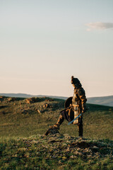 mongolian warrior with a sword standing on a hill in the sunset