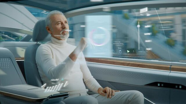 Attractive Senior Man Using Futuristic Augmented Reality Interface for Reading News and Checking Social Activity while Sitting on a Backseat of Autonomous Car. Self-Driving Van Rides on Public Road.