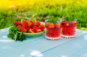 Strawberries in plate on the table and fresh drinks with mint on a sunny day
