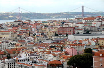 Fototapeta na wymiar Lisbon rises on the coast and is on a hilly area. From São Jorge Castle, the view is on the pastel-colored buildings of the old city, the Tagus Estuary and the 25 de Abril bridge.
