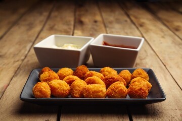 Croquettes on black plate with mayonnaise and ketchup on wooden table