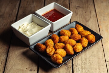 Croquettes on black plate with mayonnaise and ketchup on wooden table