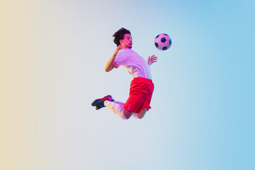 Fototapeta na wymiar Kicking in jump, on the run. Football or soccer player on gradient background in neon light - motion, action, activity. Concept of sport, competition, winning, action, motion, overcoming. Copyspace.