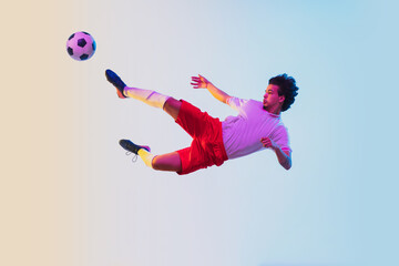 Kicking in jump, on the run. Football or soccer player on gradient background in neon light - motion, action, activity. Concept of sport, competition, winning, action, motion, overcoming. Copyspace.