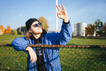 Portrait of a handsome man. A man with blue eyes looks at the camera. Fashion of the 90s. A handsome man with blond hair .The young man behind the fence .