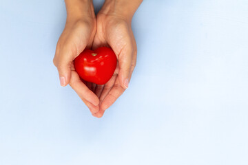 red small tomato in heart shape in hands on light blue background, empty space for text
