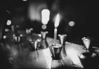 Single candle in a metal holder is burning in a church. Background image of funeral concept and...