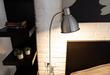 Metal Task Lamp with an adjustable reading light. Steel downbridge floor lamp with a long arm and opaque shade near bed in black and white modern bedroom. Stylish bedside lamp in scandinavian interior