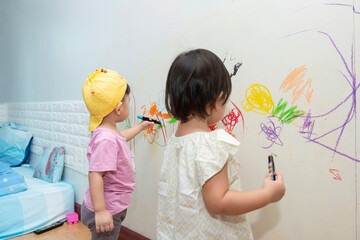  little baby  boy and girl drawing with crayon color on the wall