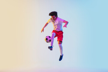 Kicking in jump, on the run. Football or soccer player on gradient background in neon light - motion, action, activity. Concept of sport, competition, winning, action, motion, overcoming. Copyspace.