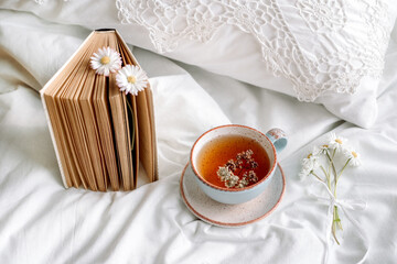Spring still life with a Cup of Natural herbal tea and flowers camomile and daisy . Light background, blooming and cozy house.White bed, summer morning