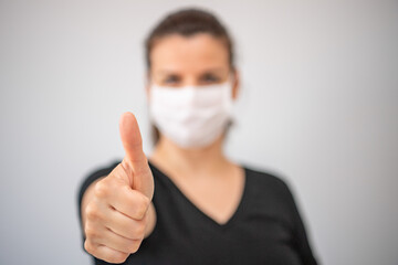 Close up portrait of beautiful brunette young  woman wearing medical  mask and showing thumb up.