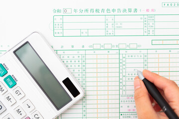 日本語で書かれた確定申告書類と白い電卓
