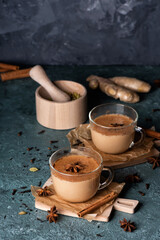 Glass cups of traditional Indian masala chai on dark green texture background. Ingredients of beverage black tea, ginger, cinnamon, cardamom, anise stars