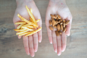 Choosing healthy or harmful food. Almond nuts or French fries in hands