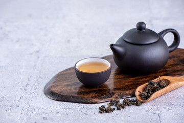 Hot tea in black teapot and cups and dry tea leaves over bright gray cement background, close up,...