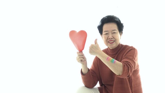 Asian elder mother support LGTBQ children thumb up smile with rainbow pride paint and red balloon heart