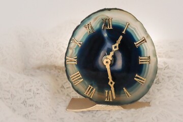 Teal agate geode table clock from Brazil with Roman numeral and golden pointers close to half past one. Soft white background with space for text. Time concept.