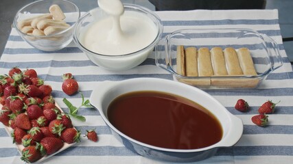 Cooking tiramisu cake at home. Young attractive housewife pours white cream on tiramisu