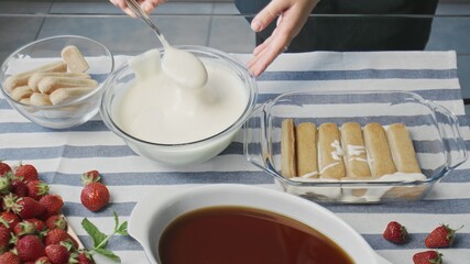 Cooking tiramisu cake at home. Young attractive housewife pours white cream on tiramisu