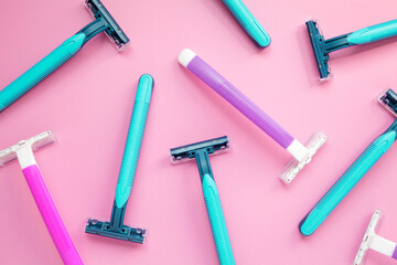 Many disposable purple and blue razors on a pink background. Colorful women and men hygiene accessories flat lay
