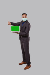 Businessman Pointing at Laptop Green Screen Isolated Wearing Medical Mask and Gloves. Indian Business man with Laptop in Hands. Online Business Concept