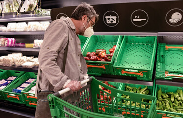 A middle-aged man with protective mask and plastic gloves drives a cart through the fruit and...