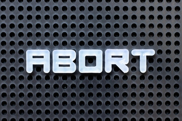 White color alphabet with word abort on black pegboard background