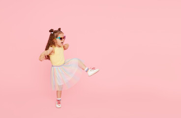 Portrait of surprised cute little toddler girl  in sunglasses over pink background.  Child model have fun and jump. Advertising childrens products - obrazy, fototapety, plakaty
