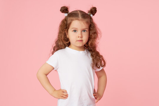 Portrait of cute european little toddler girl over pink background. Looking at camera. Child model in white T-shirt. Advertising childrens products