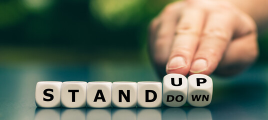 Hand turns dice and changes the expression "stand down" to "stand up".