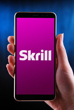 Hands holding smartphone displaying logo of Skrill