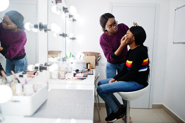 African American woman applying make-up by make-up artist at beauty saloon.