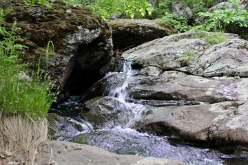 Amazing waterfall in the middle of mountain forest. River full of water during spring, beautiful flowing mass. Lovely contrast of water and surrounding forest green. Stones and fresh green leaves. 