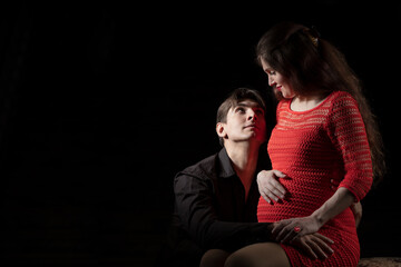 Handsome man hugs a beautiful pregnant wife on a dark background.