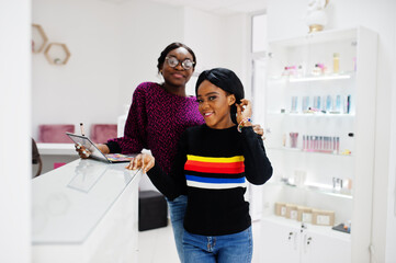 African American woman applying make-up by make-up artist at beauty saloon.