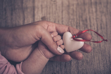 Women's hands holding the child's hand with a heart. Place for text. World humanitarian day. The concept of motherhood, caring, family, protection, love.