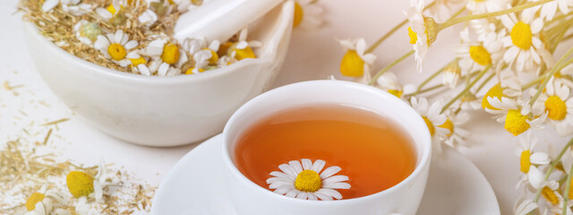 Rural still-life - cup of brewed chamomile tea on the background of a bouquet of daisies, closeup