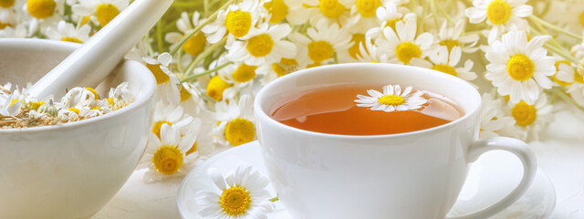 Rural still-life - cup of brewed chamomile tea on the background of a bouquet of daisies, closeup