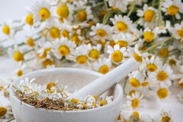 Fototapeta na wymiar Rural still-life - chamomile crushed in a mortar on the background of a bouquet of daisies, closeup