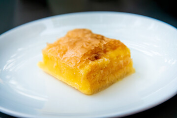 Delicious Greek sweet pastry named Galaktoboureko, made of semolina custard in filo, served with honey in white plate.