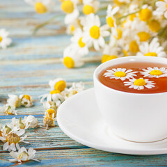 Chamomile flowers in a white cup of tea, daisy herbs on wooden background. Healthy lifestyle...