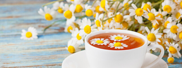 Chamomile tea, daisy flowers and a bouquet of Matricaria chamomilla on a wooden background. Herbal medicine banner.