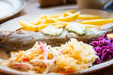 Fresh whole grilled trout served with french fries, red and white cabbage in ceramic plate