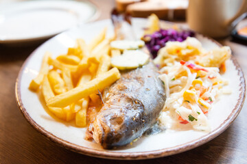 Fresh whole grilled trout served with french fries, red and white cabbage in ceramic plate