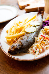 Fresh whole grilled trout served with french fries, red and white cabbage in ceramic plate